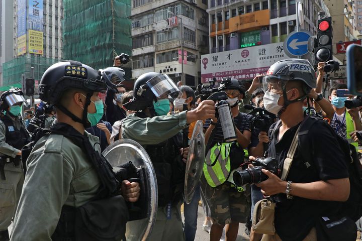 A riot police officer points pepper spray at a journalist as pro-democracy activists gather outside a shopping mall during the Labor Day in Hong Kong, Friday, May 1, 2020 amid an outbreak of the new coronavirus. (AP Photo/Kin Cheung)