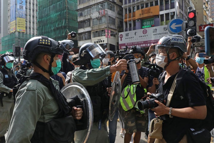 A riot police officer points pepper spray at a journalist as pro-democracy activists gather outside a shopping mall during th