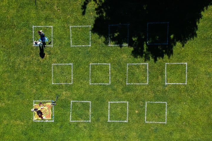 People practice social distancing sitting inside squares painted on a lawn by Vistula Boulevard in Krakow, Poland.