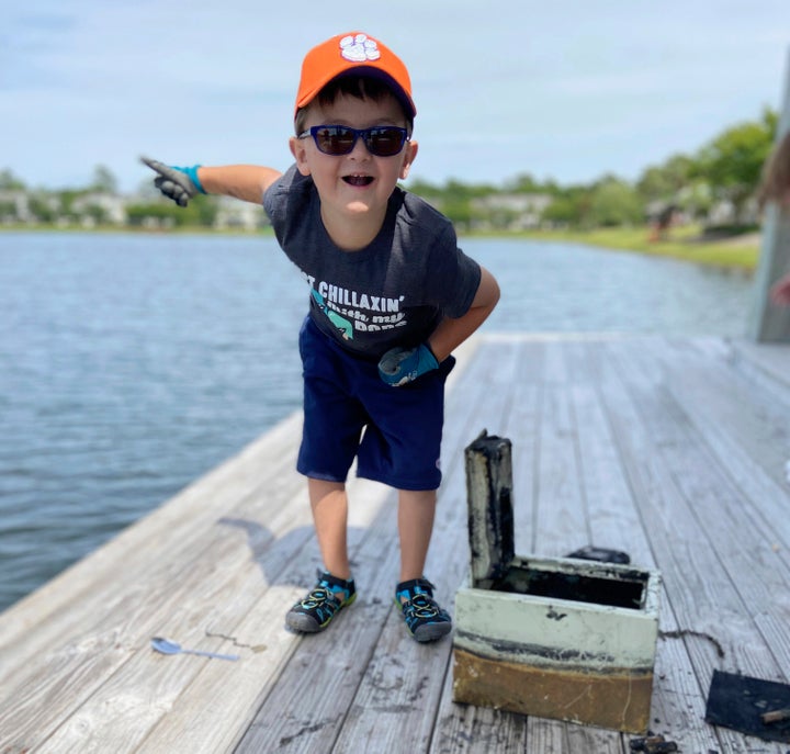 In this May 9, 2020, photo provided by Catherine Brewer, Knox Brewer stands next to a safe he pulled out of Whitney Lake in South Carolina. The 6-year-old was using a magnet attached to a string to fish for metal in the water when he reeled in a lockbox that police said was stolen from a woman who lived nearby eight years ago. (Catherine Brewer via AP)