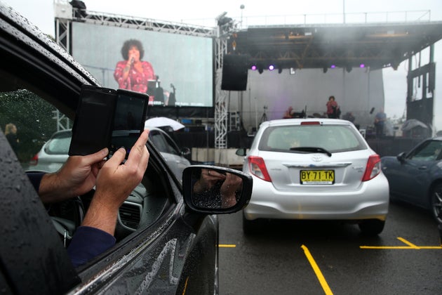 SYDNEY, AUSTRALIA - MAY 21: A man in a car takes a selfie as Casey Donovan performs on stage during a media call to showcase how a drive-in live entertainment venue will operate ahead of its opening in July in the suburb of Tempe on May 21, 2020 in Sydney, Australia. From July visitors will be able to drive to the venue and enjoy music and performances from the safety of their vehicles as restrictions on group sizes continues due to the COVID-19 pandemic. (Photo by Don Arnold/WireImage)