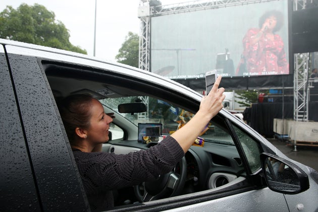 SYDNEY, AUSTRALIA - MAY 21: A girl in a car takes a selfie as Casey Donovan performs on stage during a media call to showcase how a drive-in live entertainment venue will operate ahead of its opening in July in the suburb of Tempe on May 21, 2020 in Sydney, Australia. From July visitors will be able to drive to the venue and enjoy music and performances from the safety of their vehicles as restrictions on group sizes continues due to the COVID-19 pandemic. (Photo by Don Arnold/WireImage)