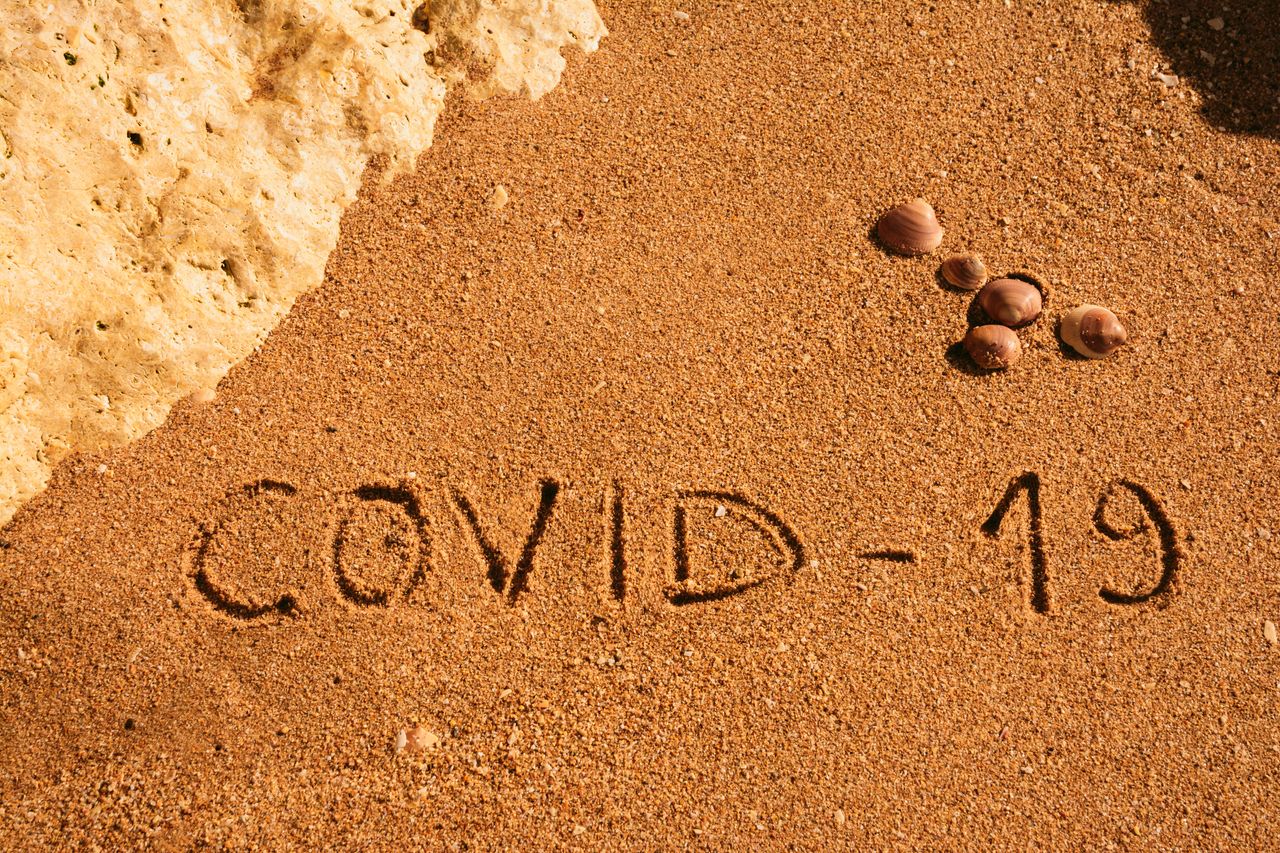 Travel and tourism concept for pandemic alert, flights and trips cancellation. Text written on the sandy beach in Algarve.