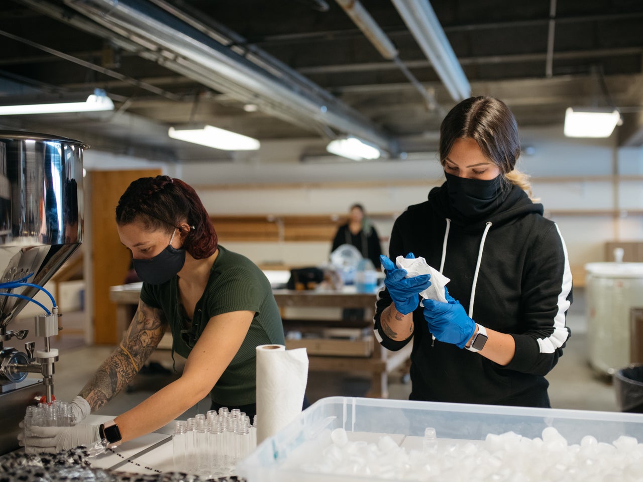 Amanda Halverson, left, fills bottles of hand sanitizer from a pneumatic filler while Makayla Deppa readies caps for the capping machine.