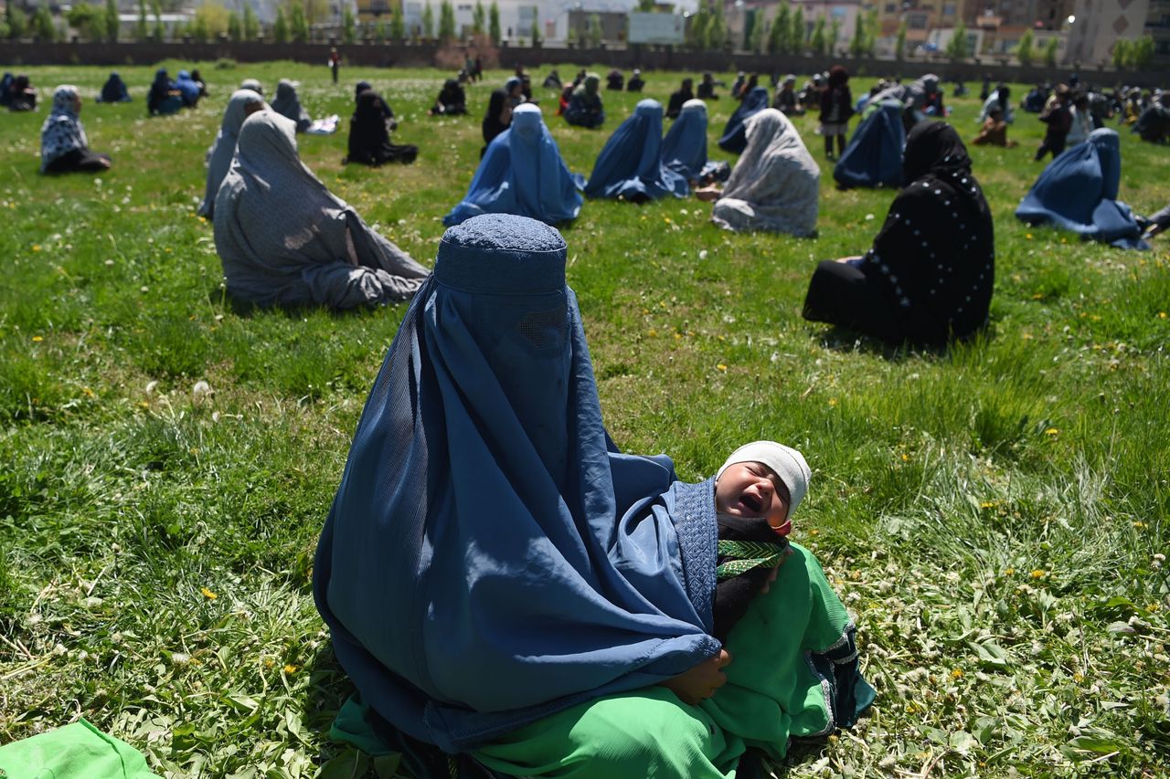 Γυναίκα με μπούργκα κρατά στην αγκαλιά ένα μωρό καθώς περιμένει να λάβει δωρεάν δημητριακά από κρατικές υπηρεσίες του Αφγανιστάν, εν μέσω πανδημίας