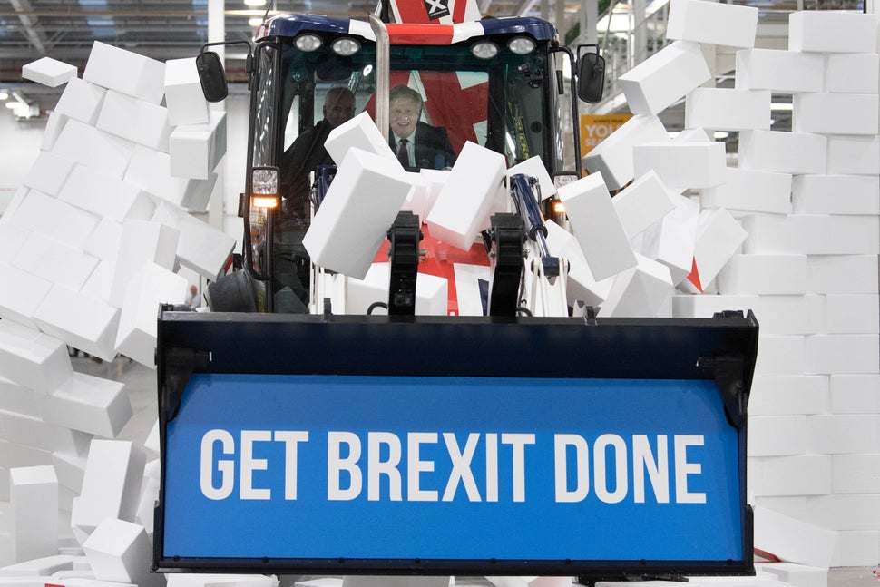 Johnson driving a Union flag-themed JCB, with the words "Get Brexit Done" inside the digger bucket, through a fake wall embla