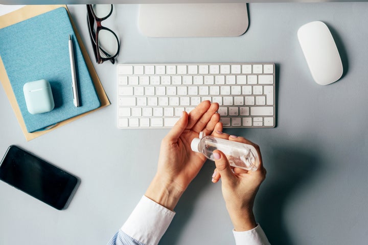 Close-up of hands using antiseptic gel to disinfect hands over a work desk in an office. Preventive measures during the period of epidemic and social exclusion.