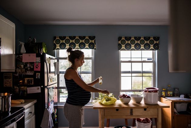 Expectant mother shucking corn in brightly lit kitchen