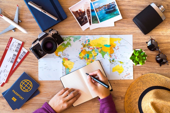 Woman making a list for her travel, on a wooden desktop with travel accessories.