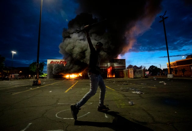 A man poses for a photo in the parking lot of an AutoZone store in flames, while protesters hold a rally for George Floyd in Minneapolis on Wednesday. 