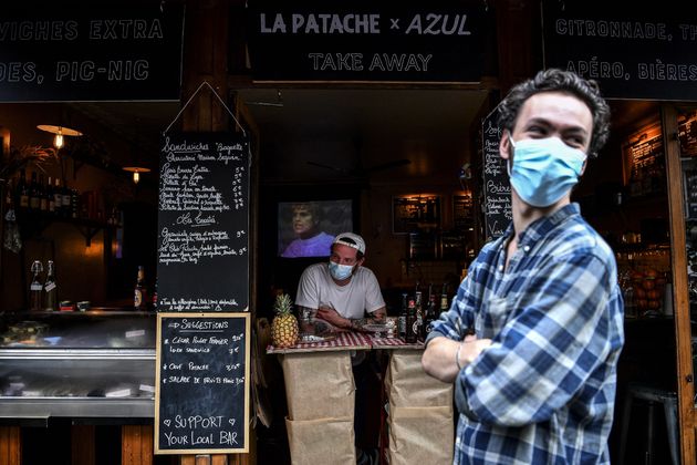 A bartender selling take-away drinks and food waits for customers behind a makeshift counter along the...