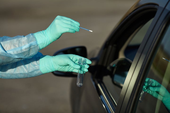 Epidemic concept COVID-19. Coronavirus Test Station. Medical worker in full protective gear takes sample from patient at a COVID-19 drive-thru test site. Testing is done by throat swab.