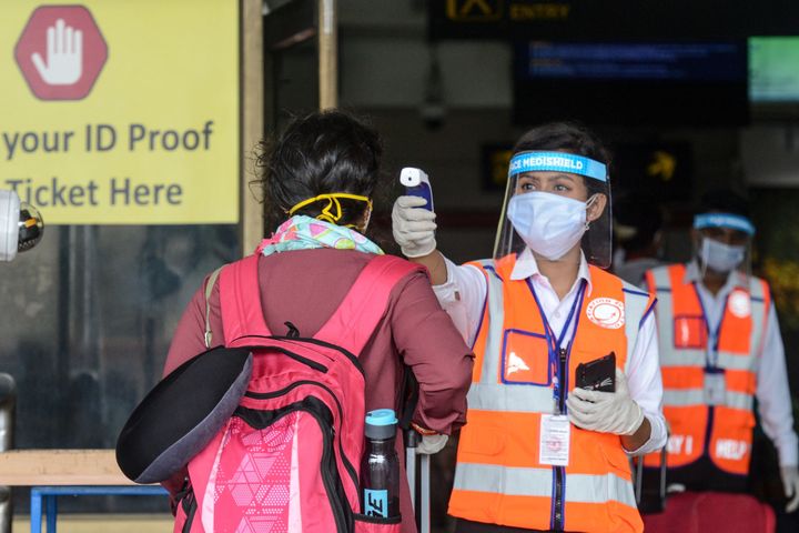 An airport employee wearing a face shield checks the body temperature of a passenger at Bagdogra airport on the outskirts of Siliguri on May 28, 2020.