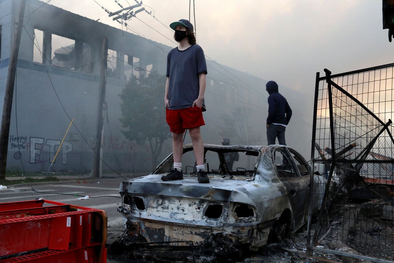 People stand on a burned up car as fires burn near a Target Store early Thursday.