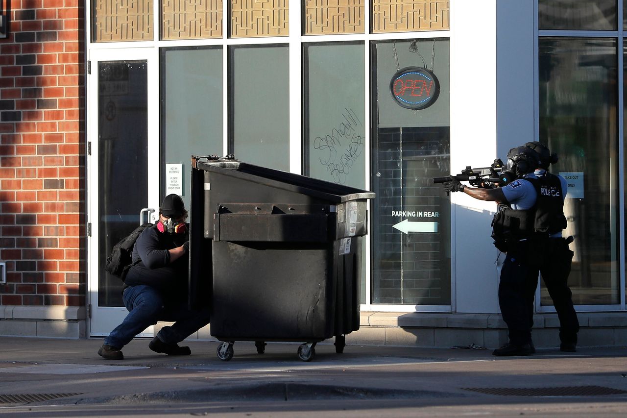 A protester hides behind a dumpster he pulled as a barrier while St. Paul Police officers move in to retrieve it.