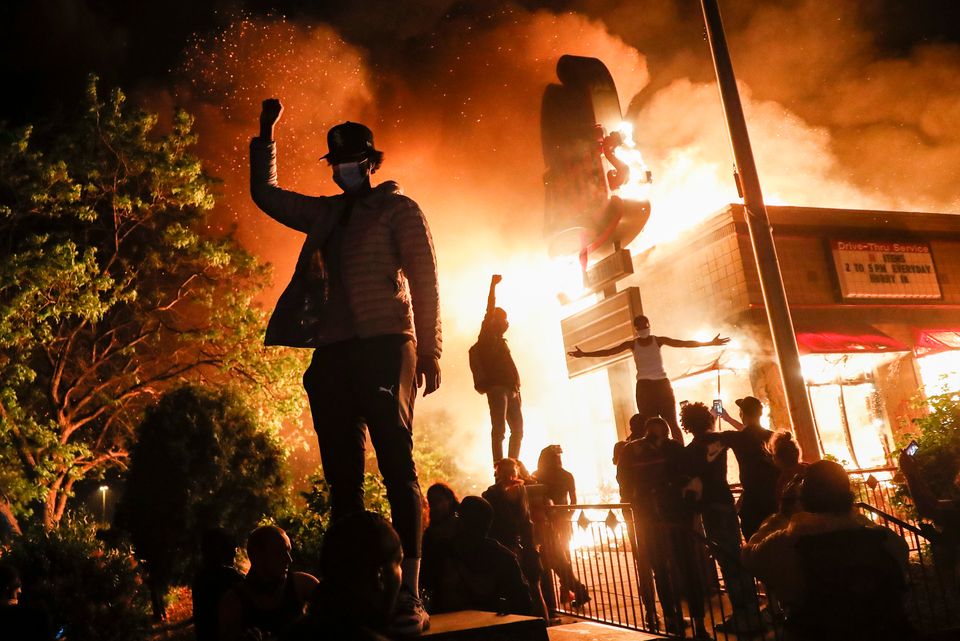 Protestors demonstrate outside of a burning fast food restaurant.