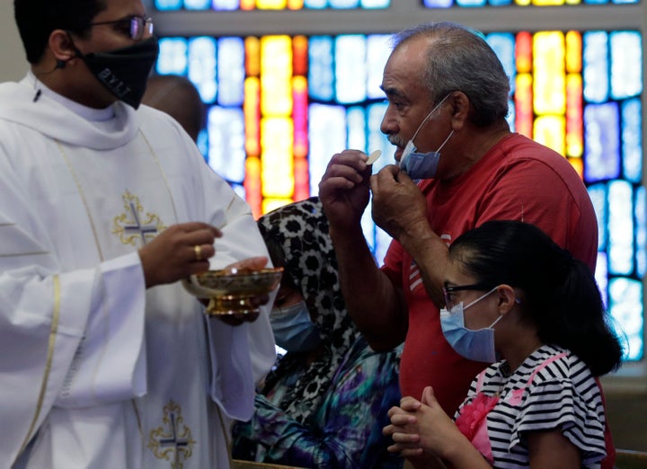 The Rev. Praveen Lakkisettit, left, wears a face mask as he delivers communion to parishioners during an in-person Mass at Christ the King Catholic Church in San Antonio, Tuesday, May 19, 2020.