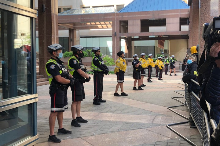 Toronto police officers form a barricade outside their downtown headquarters as protesters gather around on May 30, 2020.