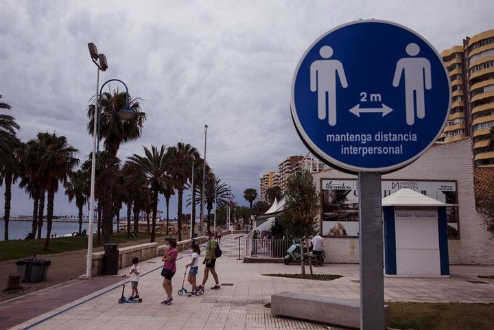 Una familia en el paseo marítimo de la Malagueta (Málaga) ante un disco que recuerda mantener la distancia de 2 metros entre personas, este domingo.
