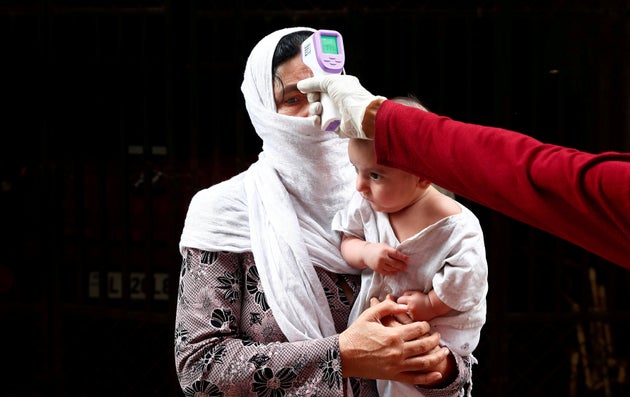 A health worker scans a resident with an infrared thermometer to check her temperature at a residential...