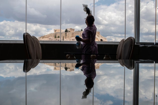 Hotel worker Mailinda Kaci cleans the windows in a restaurant area at the Acropolian Spirit Hotel in central Athens as the ancient Acropolis is seen in the background, on Monday June 1, 2020. Lockdown restrictions were lifted on non-seasonal hotels Monday as the country prepares to start its tourism season on June 15. (AP Photo/Petros Giannakouris)