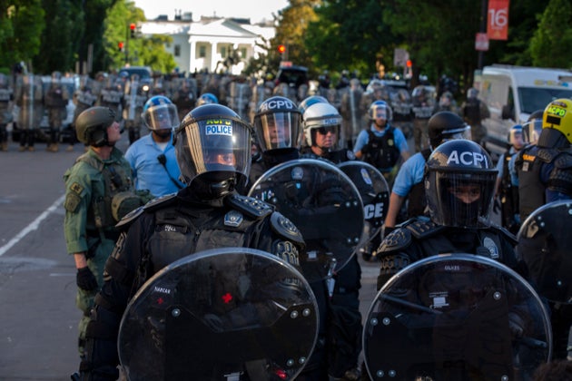 The White House looms in the background behind a line of law enforcement officers wearing riot gear as...