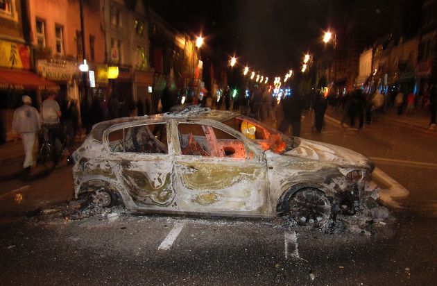 People gather near the remains of a police patrol car left after being set on fire during a protest in Tottenham.