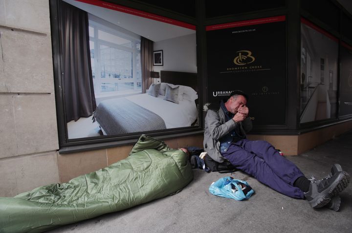 People sleeping rough next to a display advertising luxury apartments, in Victoria, London.