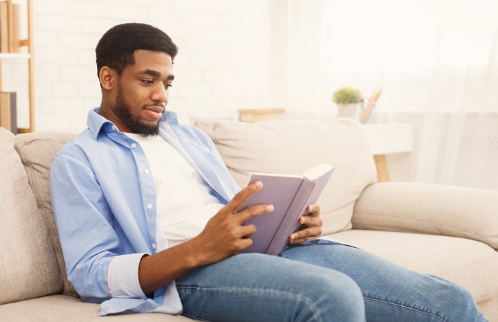 Relaxed african-american man reading book, having rest at home, copy space