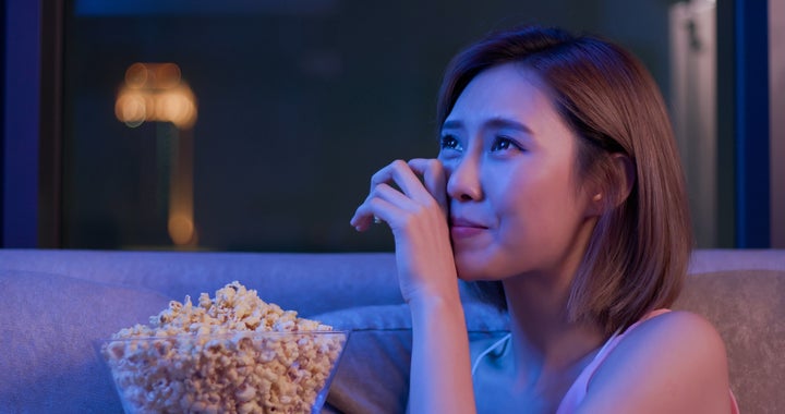 Young woman cry while watching a very touching movie with popcorn at night