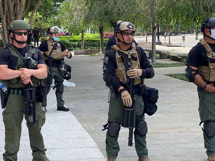 Federal law enforcement officers wear unidentifiable uniforms, some with plain T-shirts under their military-style gear, whil