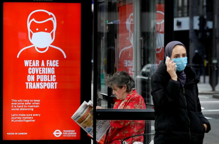 Passengers wait at a bus stop with a sign advising travellers to wear a face covering whilst travelling, in London, Friday June 5