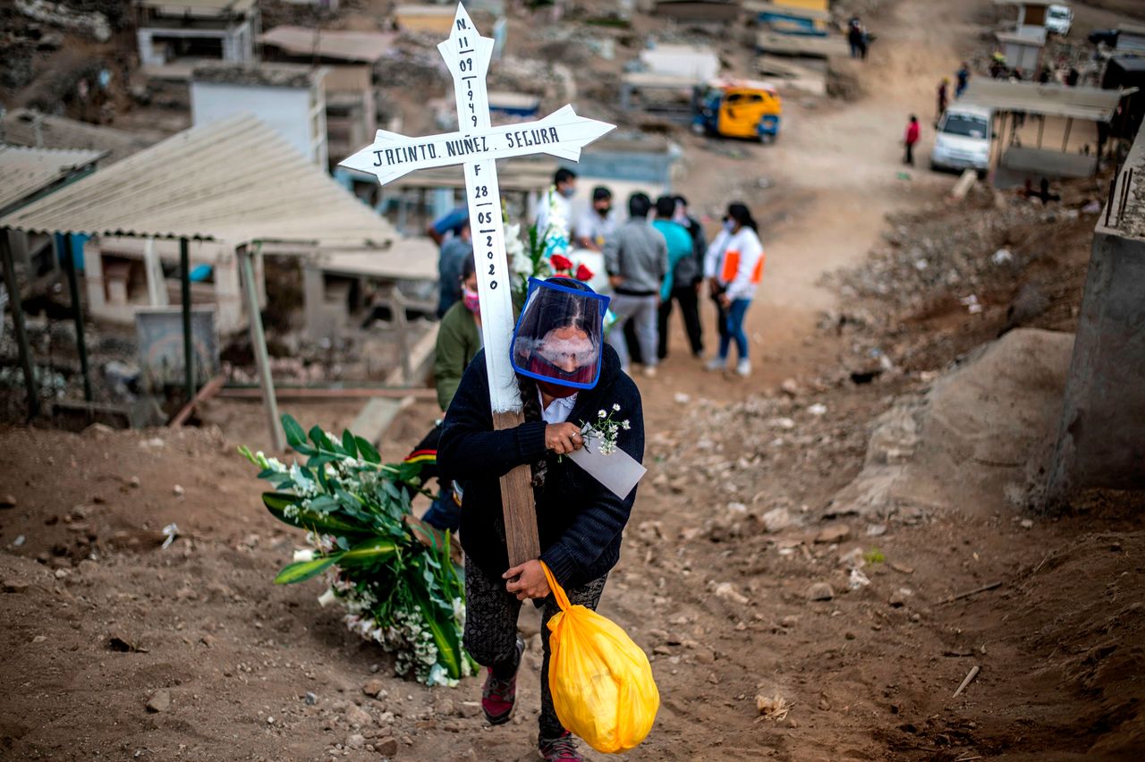 Συγγενής νεκρού που έχασε την μάχη με τον κορονοϊό, μεταφέρει ένα σταυρό κατά την διάρκεια της κηδείας, στο νεκροταφείο Νουέβα Εσπεράντσα. Πρόκειται για ένα από τα μεγαλύτερα νεκροταφεία της Λατινικής Αμερικής, στα περίχωρα της Λίμα, στο Περού. Σάββατο 30 Μαίου.