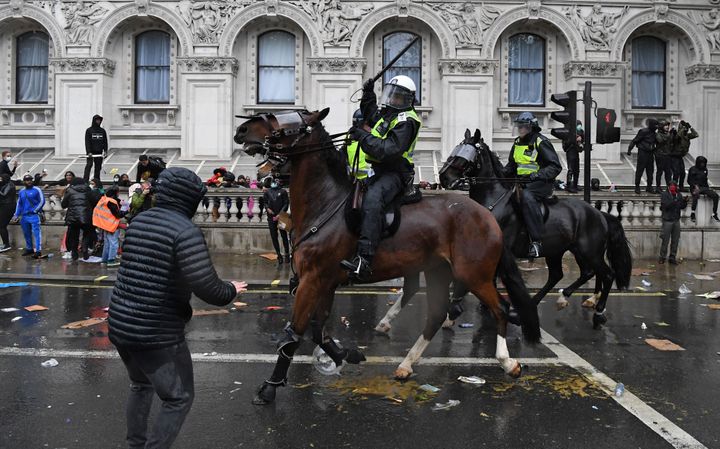A mounted police officer raises their baton as police horses ride along Whitehall in an attempt to disperse protesters.