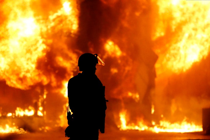 A Minneapolis Police officer stands near a structure fire, Saturday, May 30, 2020, in Minneapolis. Protests continued following the death of George Floyd, who died after being restrained by Minneapolis police officers on Memorial Day. (AP Photo/Julio Cortez)