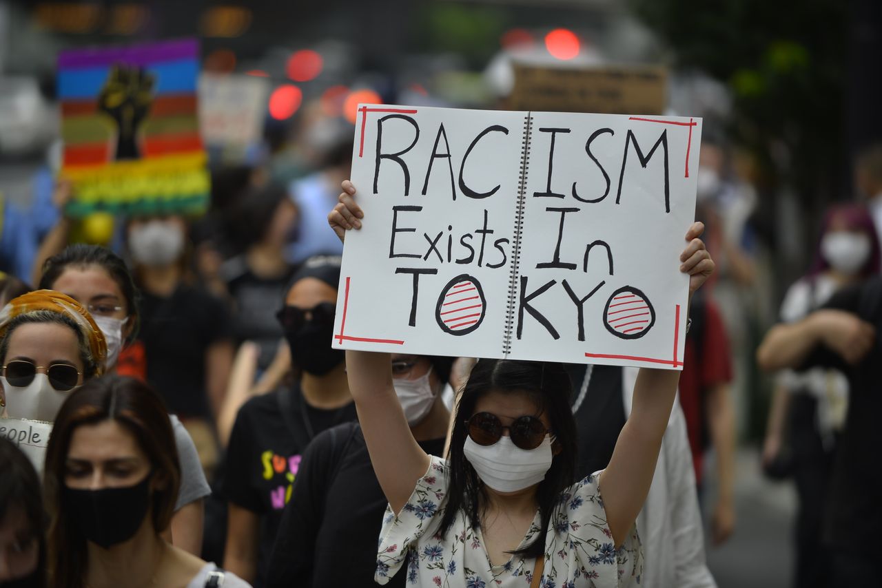 A demonstrator holds up a sign that reads "Racism exists in Tokyo" at a Saturday protest in Tokyo.