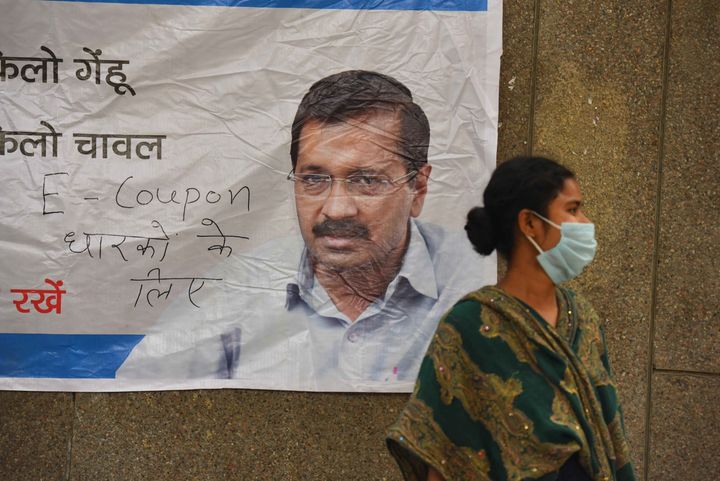 A woman wearing facemask seen next to a poster of Delhi Chief Minister Arvind Kejriwal during a community feeding session on day sixteen of the 21 days nationwide lockdown to curb the spread of Coronavirus, at New Ashok Nagar on April 9, 2020 in New Delhi, India. 