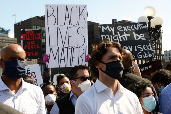 A protester holds up a Black Lives Matter sign behind Prime Minister Justin Trudeau during an anti-racism protest on Parliament on June 5, 2020.
