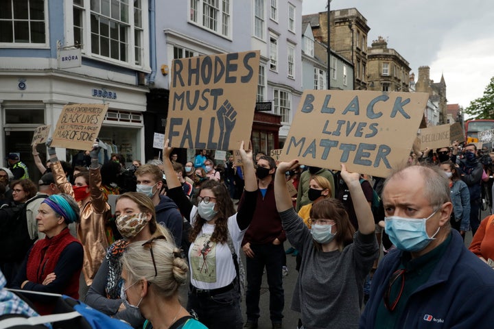 Supporters of the Rhodes Must Fall group, wearing protective masks against the spread of coronavirus, participate in a protest calling for the removal of a statue of Cecil Rhodes, a Victorian imperialist in southern Africa who made a fortune from mines and endowed the university's Rhodes scholarships, beneath the statue which stands on the facade of Oriel College, in Oxford, England, Tuesday, June 9, 2020. More statues of imperialist figures could be removed from Britain's streets, following the toppling of a monument to slave trader Edward Colston in the city of Bristol, the mayor of London said Tuesday. (AP Photo/Matt Dunham)