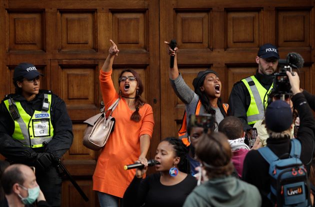 Supporters of the Rhodes Must Fall group chant slogans during a protest calling for the removal of a statue of Cecil Rhodes, a Victorian imperialist in southern Africa who made a fortune from mines and endowed the university's Rhodes scholarships, beneath the statue which stands on the facade of Oriel College, in Oxford, England, Tuesday, June 9, 2020. More statues of imperialist figures could be removed from Britain's streets, following the toppling of a monument to slave trader Edward Colston in the city of Bristol, the mayor of London said Tuesday. (AP Photo/Matt Dunham)