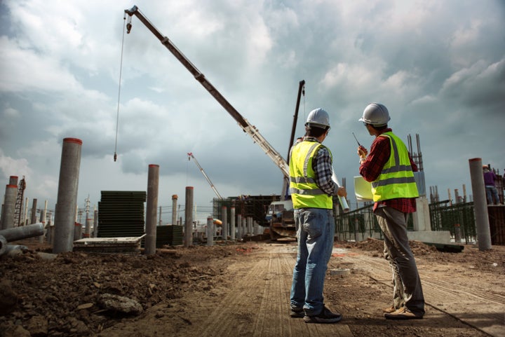 Construction engineers discussion with consultant people at construction site of highrise building with blueprints.