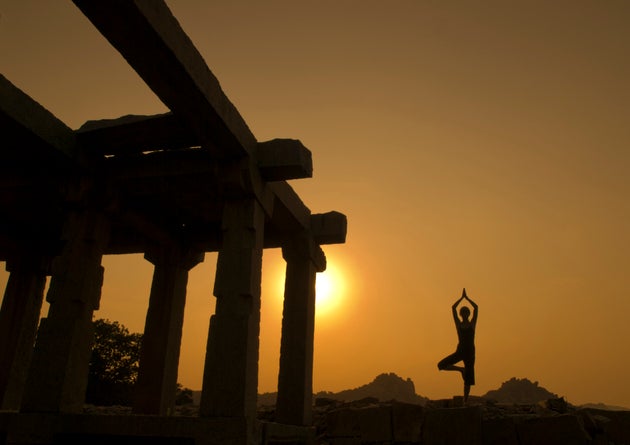India, Karnataka, Hampi, Silhouette of woman doing yoga near temple at sunset