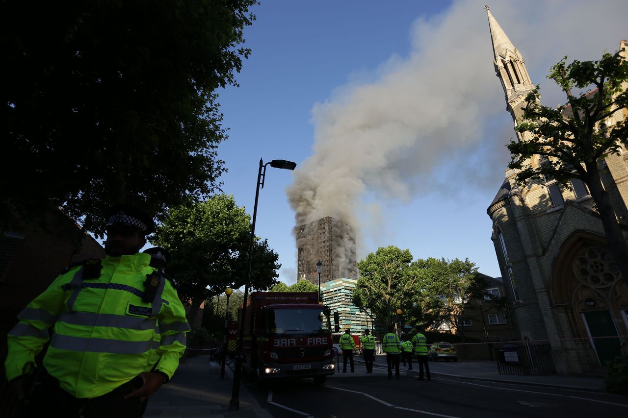 Police patrol a security cordon as smoke billows from Grenfell Tower