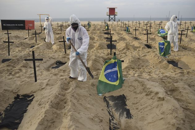 Manifestantes, usando equipamento de proteção, cavam túmulos simulados na praia de Copacabana, simbolizando as mortes devido ao coronavírus no Rio.