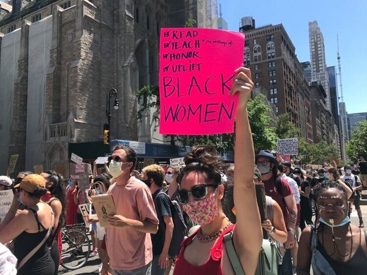「BLACK WOMEN」というピンク色のサインを掲げて行進する女性