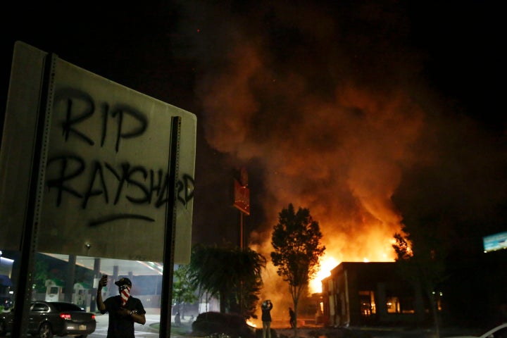 "RIP Rayshard" is spray painted on a sign as as flames engulf a Wendy's restaurant during protests Saturday, June 13, 2020, in Atlanta. The restaurant was where Rayshard Brooks was shot and killed by police Friday evening following a struggle in the restaurant's drive-thru line. (AP Photo/Brynn Anderson)