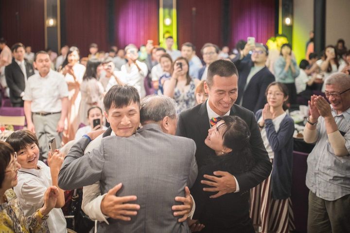 結婚式で友人らが見守る中、家族と抱き合う有吉英三郎さん（右）とパートナーの盧盈任さん