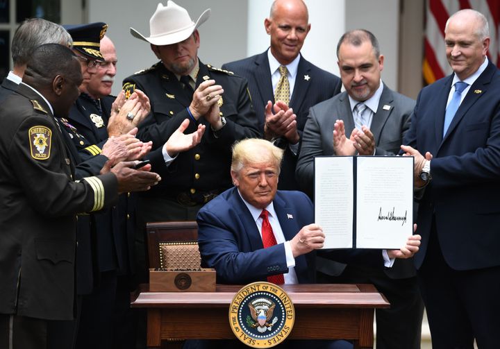 Surrounded by law enforcement officials, President Donald Trump shows his signature on an executive order on Safe Policing for Safe Communities in the Rose Garden of the White House On Tuesday.