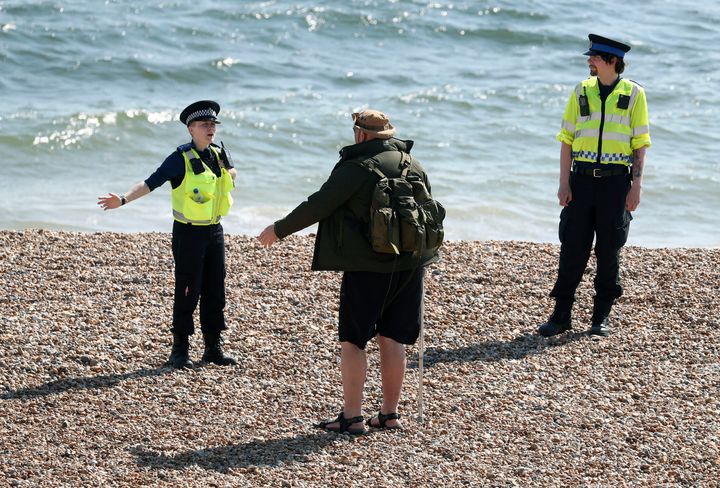 Police officers speak to a man as they patrol the beach in Brighton during the lockdown