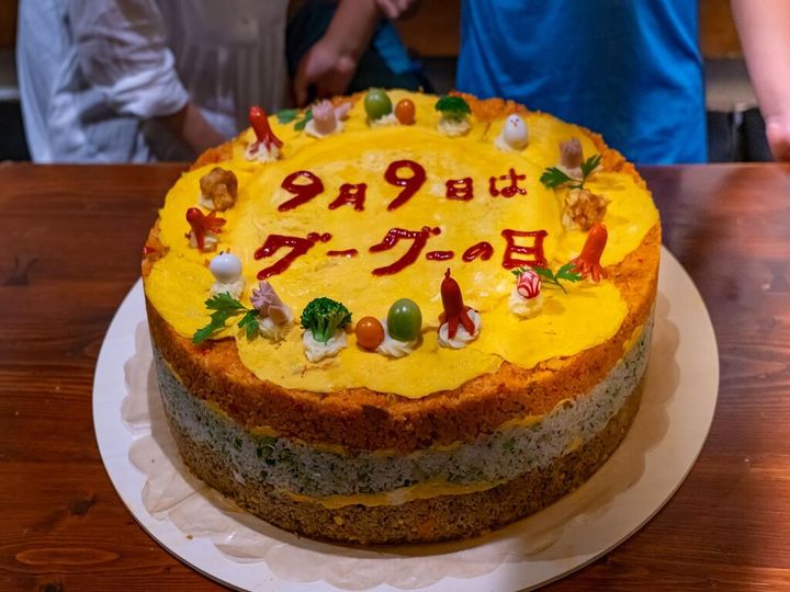 イベントの目玉、直径50cm、高さ11cmの「具ー具ーだくさんオムライスケーキ」！筆者考案、飯島奈美氏制作。みなと子ども食堂ボランティアの皆さまと。